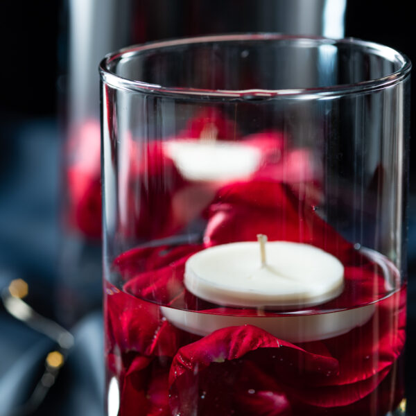 Wazon szklany udekorowany świecą i płatkami róż